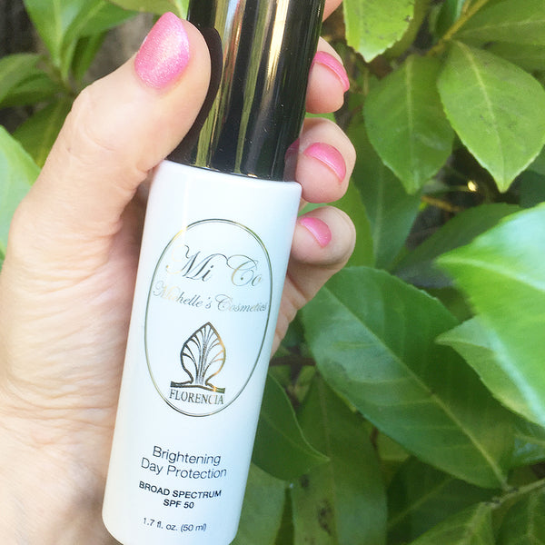 Hand holding a bottle of SPF 50 Brightening Day Protection Broad Spectrum.