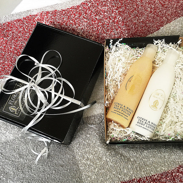 Black gift wrap box opened with two bottles resting on shredded paper for cushioning.